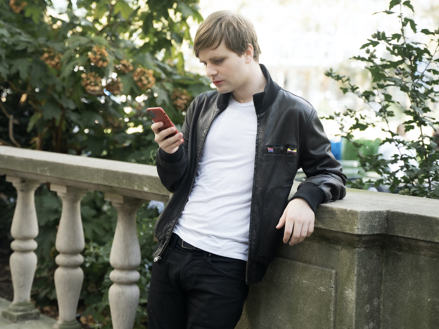 Photo of Matthew Bischoff looking at their phone waring a leather jacket in a park.